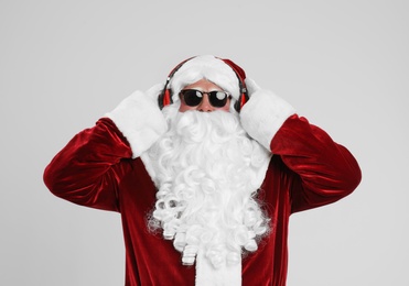 Photo of Santa Claus with headphones listening to Christmas music on light grey background