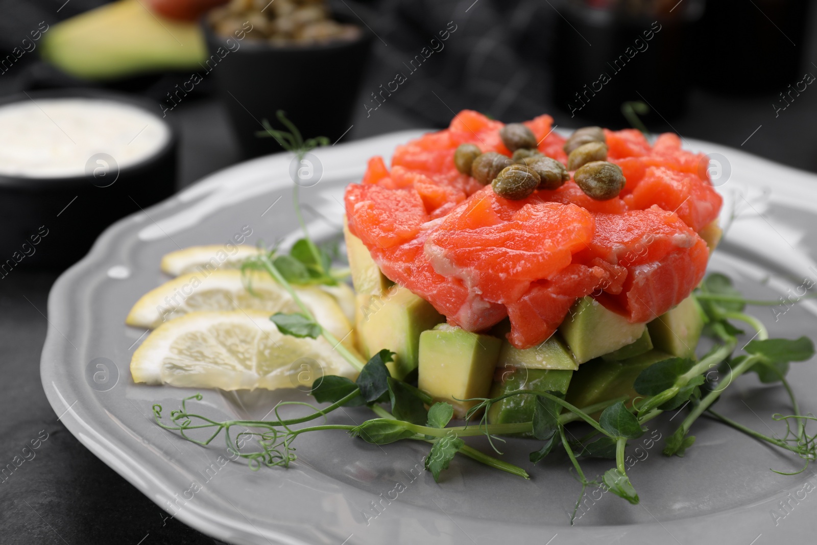 Photo of Delicious salmon tartare served with avocado and lemon on dark table, closeup