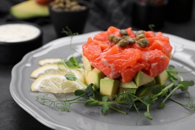 Delicious salmon tartare served with avocado and lemon on dark table, closeup