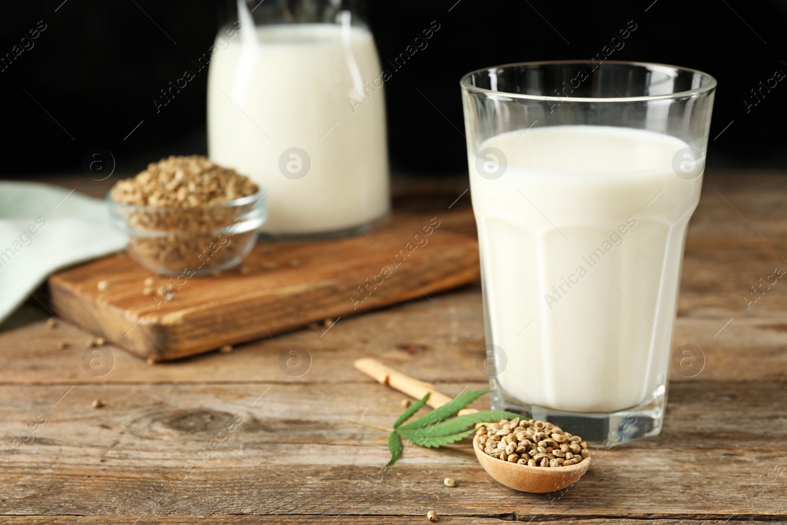 Photo of Composition with glass of hemp milk on wooden table against black background. Space for text