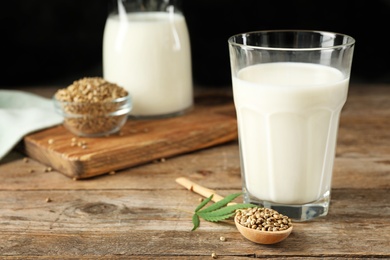 Composition with glass of hemp milk on wooden table against black background. Space for text