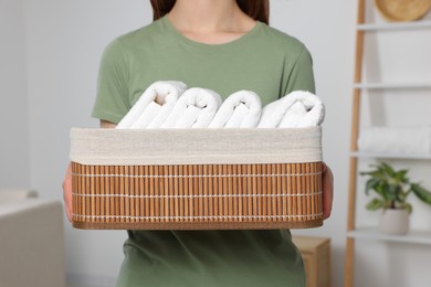 Photo of Woman holding wicker basket with folded soft terry towels indoors, closeup