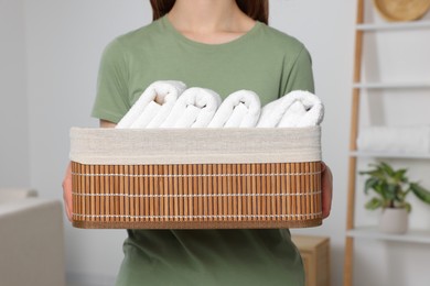 Woman holding wicker basket with folded soft terry towels indoors, closeup