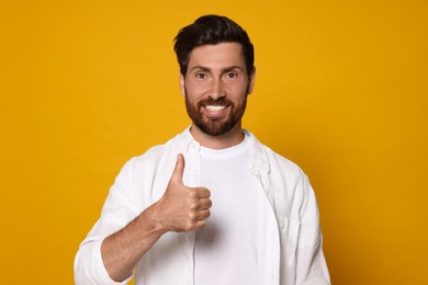 Photo of Handsome bearded man showing thumb up on orange background
