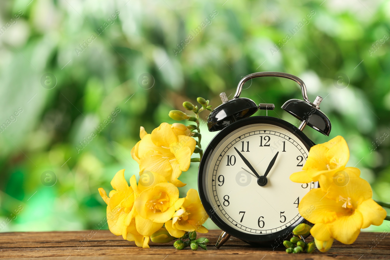 Photo of Alarm clock and beautiful spring flowers on wooden table. Time change concept