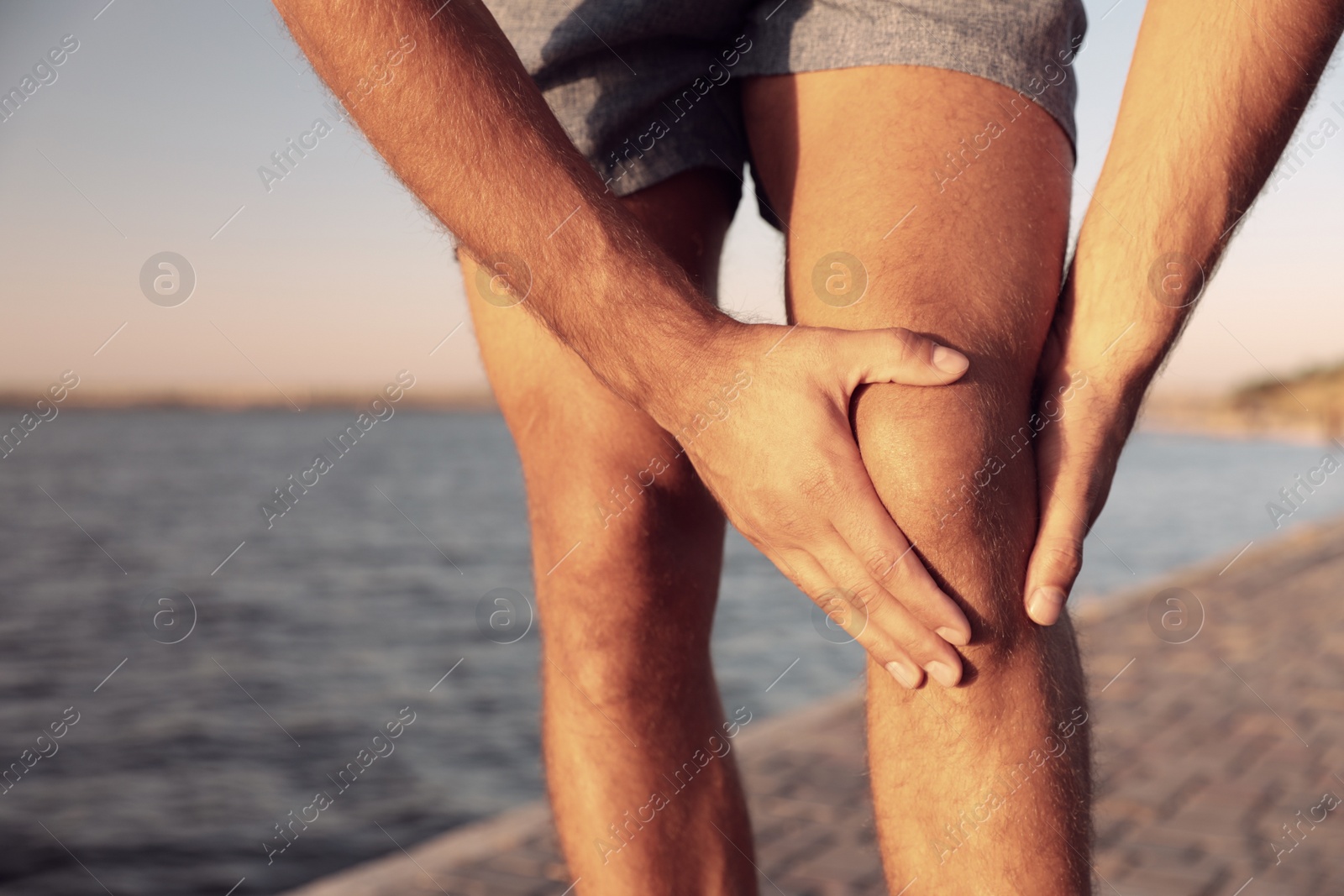 Photo of Man having knee problems near river at sunset, closeup