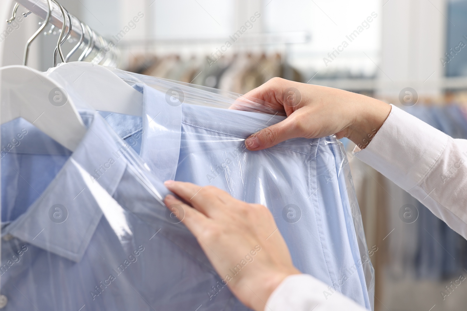 Photo of Dry-cleaning service. Woman taking shirt in plastic bag from rack indoors, closeup