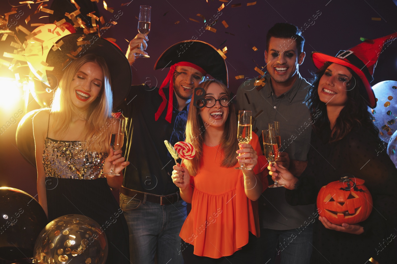 Photo of Happy friends in costumes enjoying Halloween party on dark background