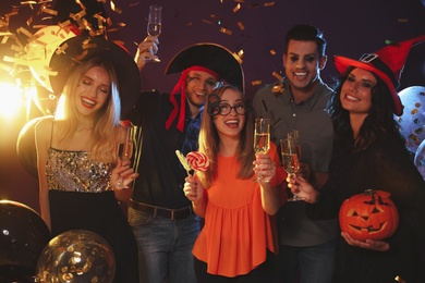 Photo of Happy friends in costumes enjoying Halloween party on dark background