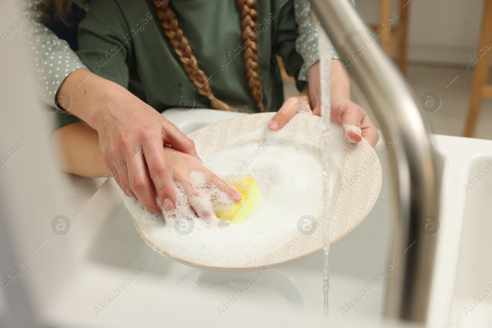 Photo of Mother and daughter washing plate above sink indoors, closeup