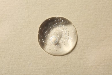 Photo of Drop of cosmetic serum on beige background, top view