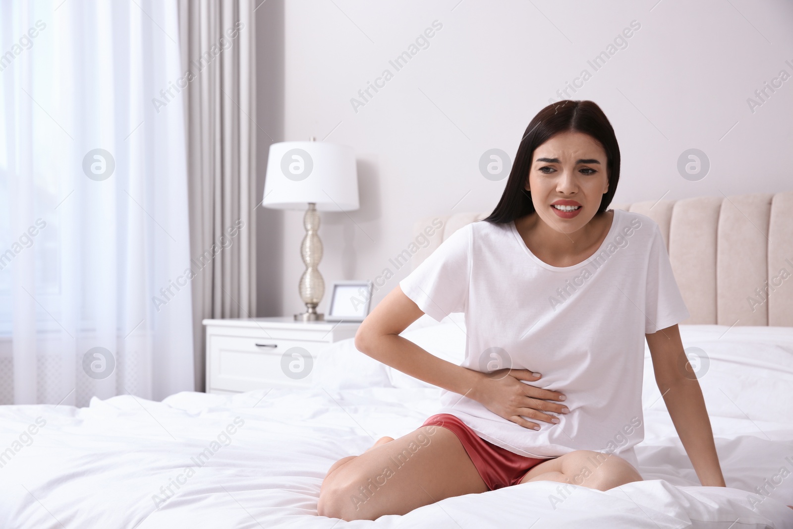 Photo of Young woman suffering from stomach ache in bedroom