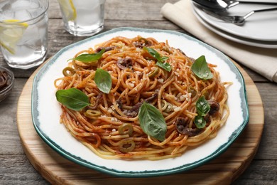 Photo of Delicious pasta with anchovies, tomato sauce and basil on wooden table
