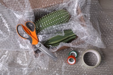 Ceramic cacti with bubble wrap in cardboard box, scissors and adhesive tapes on wooden table, above view