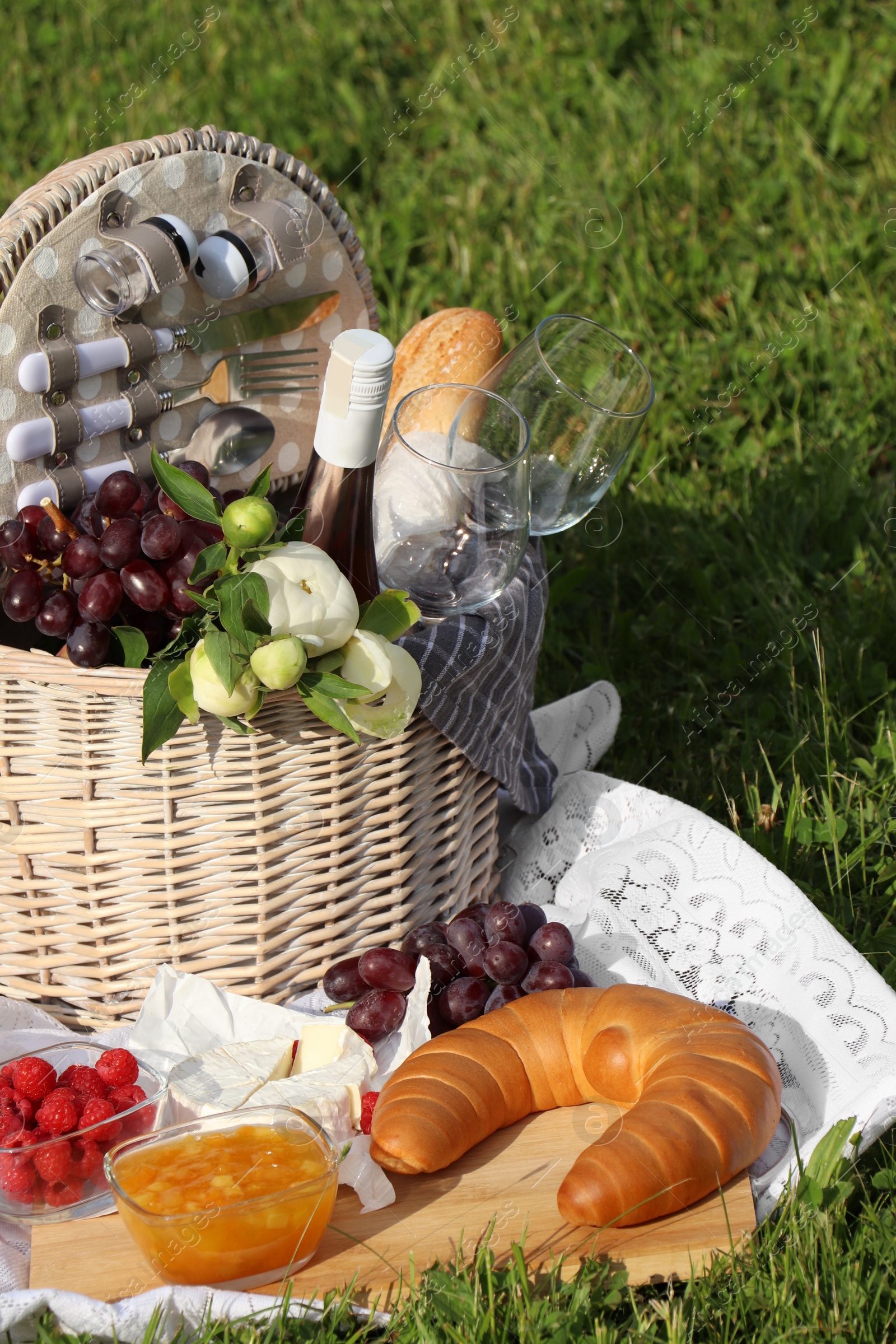 Photo of Picnic blanket with tasty food, flowers, basket and cider on green grass outdoors