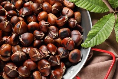 Photo of Delicious roasted edible chestnuts in frying pan on table, top view
