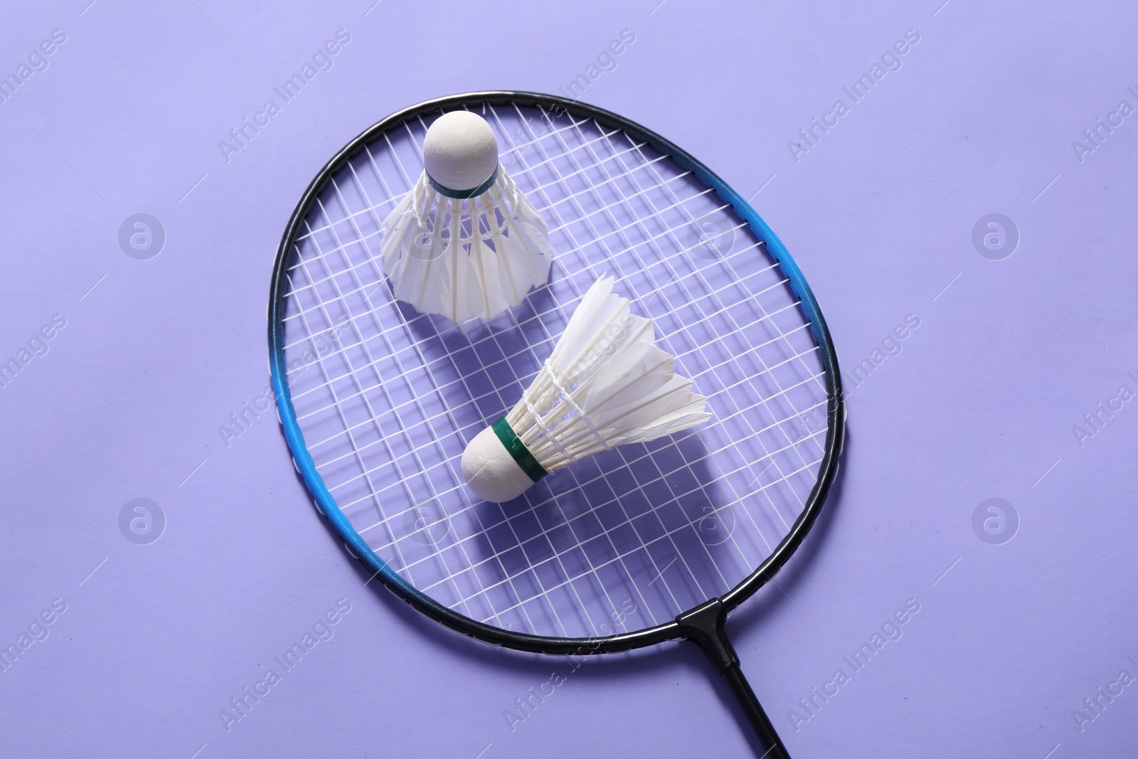 Photo of Feather badminton shuttlecocks and racket on violet background, top view