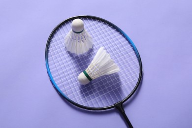 Feather badminton shuttlecocks and racket on violet background, top view