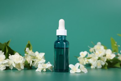 Photo of Essential oil in bottle and beautiful jasmine flowers on green background