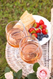 Photo of Glasses of delicious rose wine and food on picnic basket outdoors