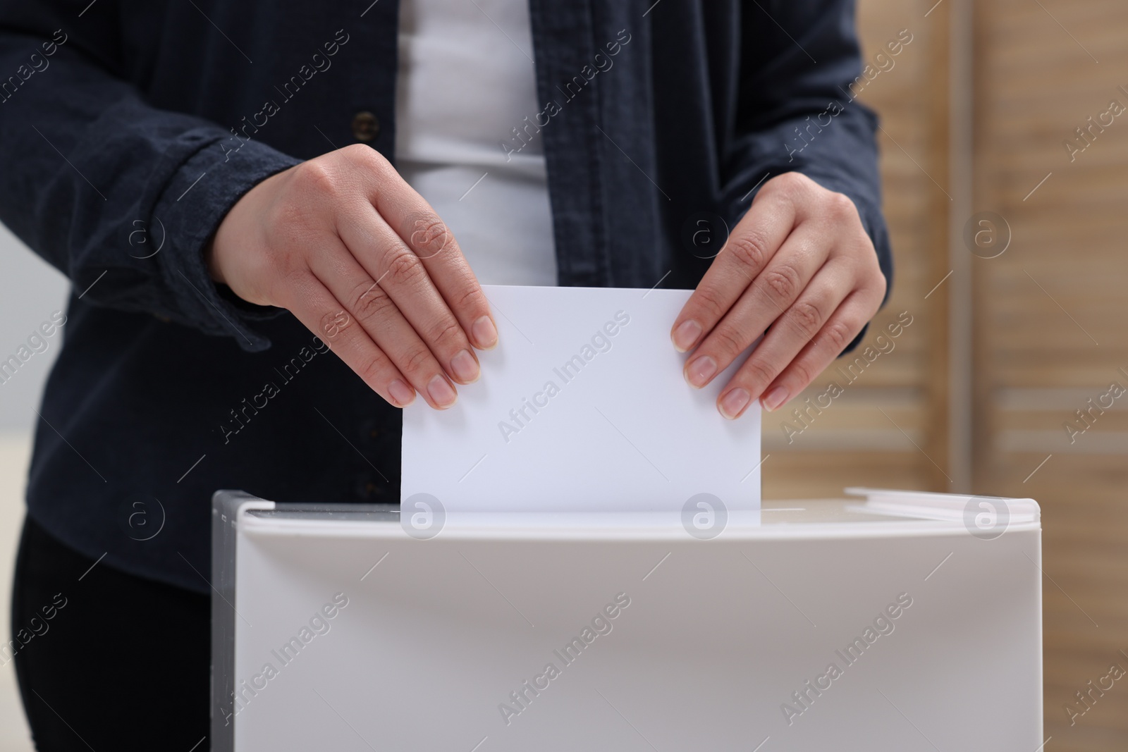 Photo of Woman putting her vote into ballot box on blurred background, closeup