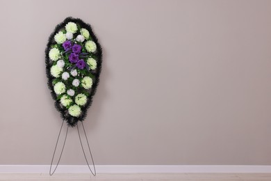 Photo of Funeral wreath of plastic flowers near grey wall indoors. Space for text