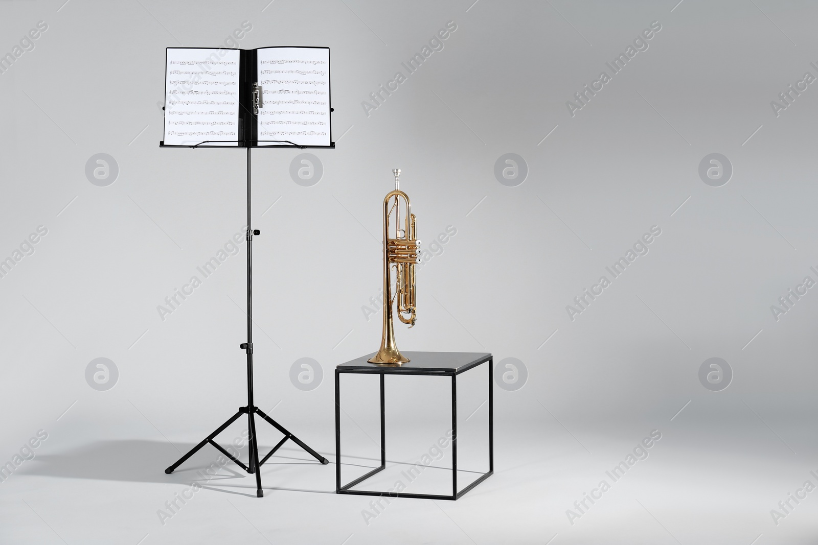 Photo of Trumpet and note stand with music sheets on grey background. Space for text