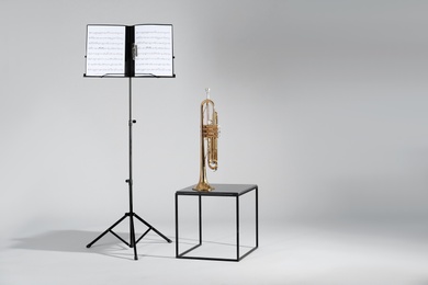 Photo of Trumpet and note stand with music sheets on grey background. Space for text