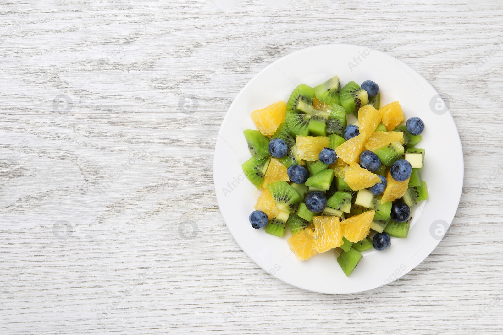Photo of Plate of tasty fruit salad on white wooden table, top view. Space for text