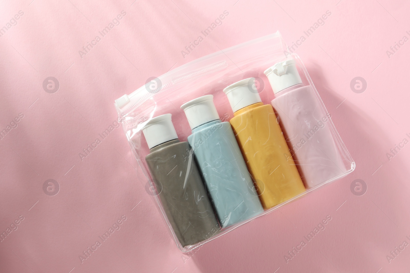 Photo of Cosmetic travel kit in plastic bag on pink background, top view