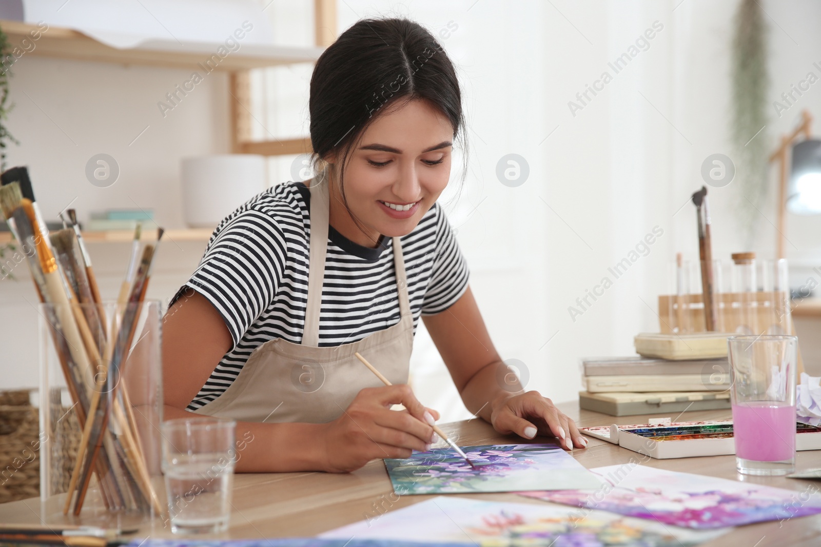 Photo of Young woman drawing flowers with watercolors at table indoors