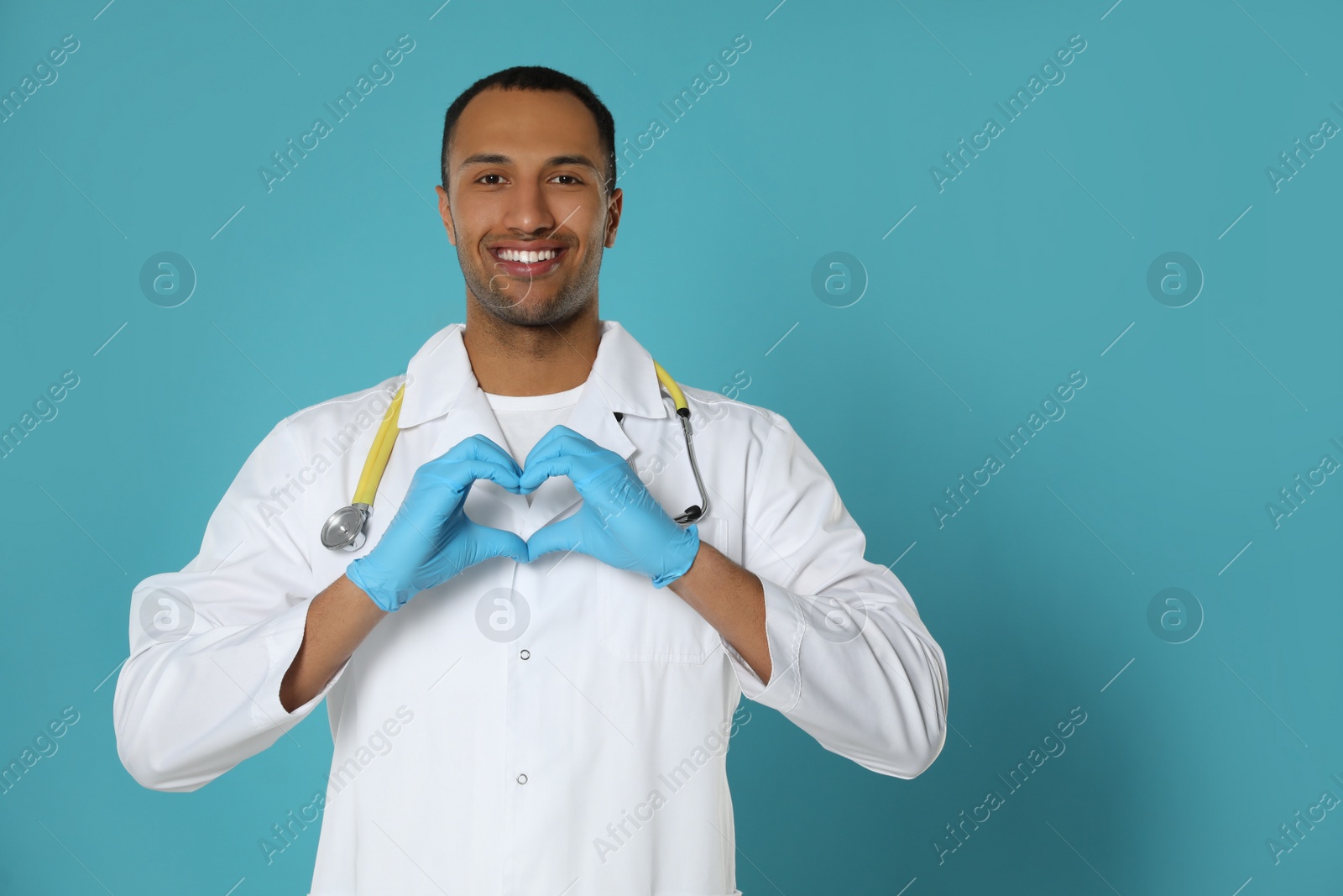 Photo of Doctor or medical assistant (male nurse) in uniform making heart with hands turquoise background. Space for text