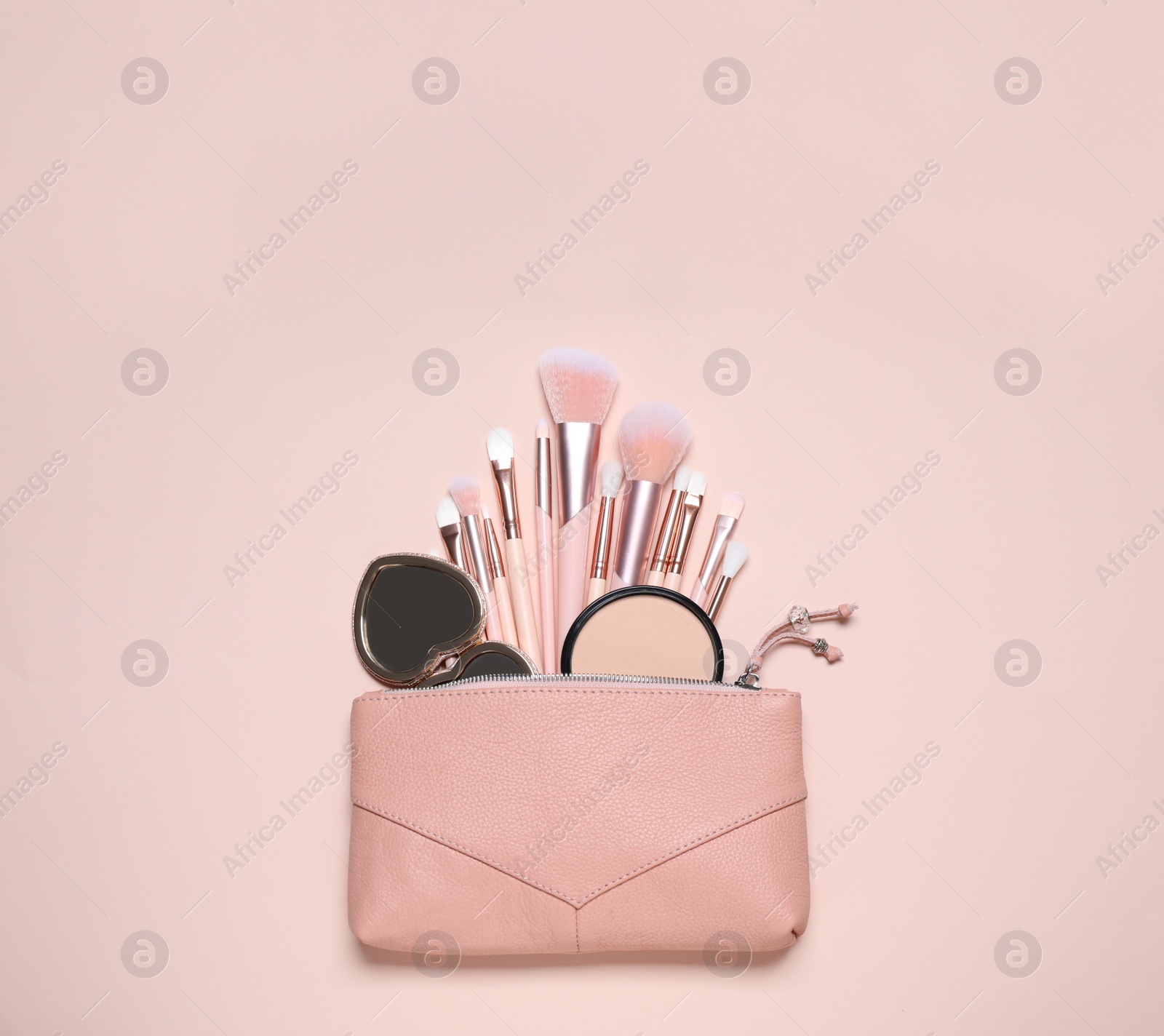 Photo of Makeup brushes, powder and mirror in cosmetic bag on pink background, flat lay