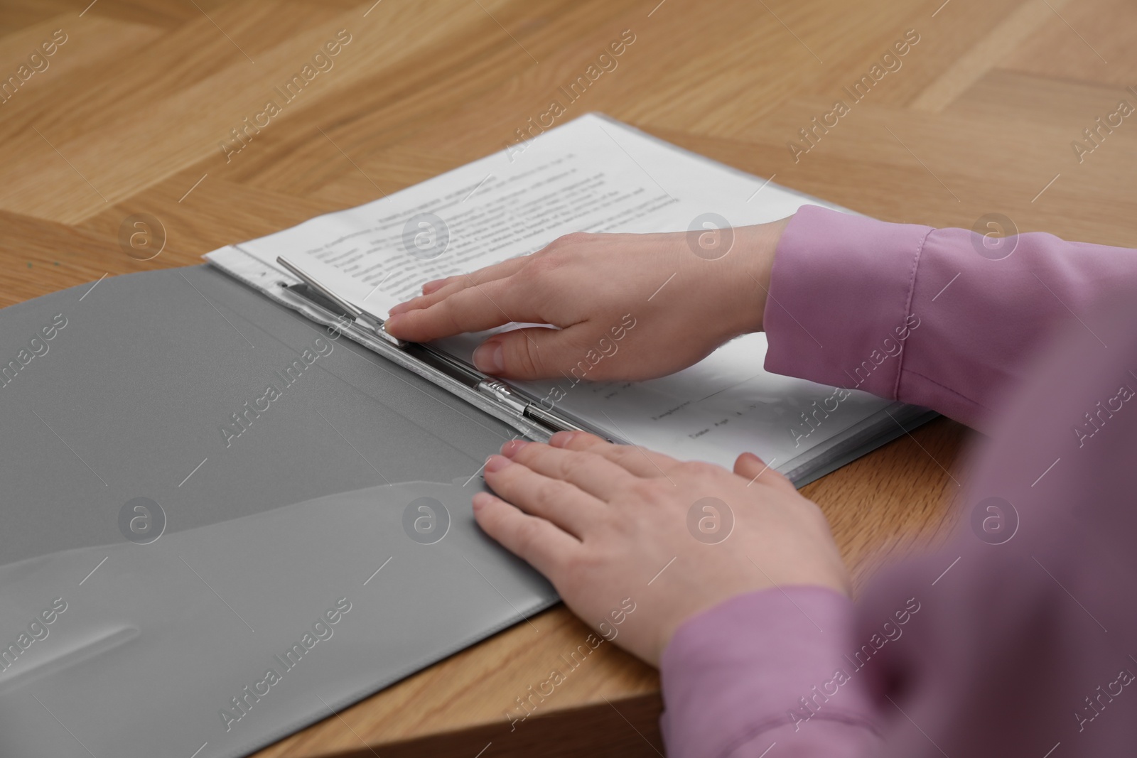 Photo of Woman fixing folder with punched pockets at wooden table, closeup