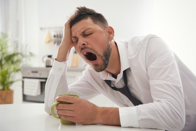 Photo of Sleepy man with cup of drink at home in morning