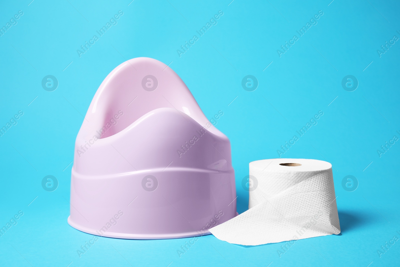 Photo of Pink baby potty and toilet paper on light blue background