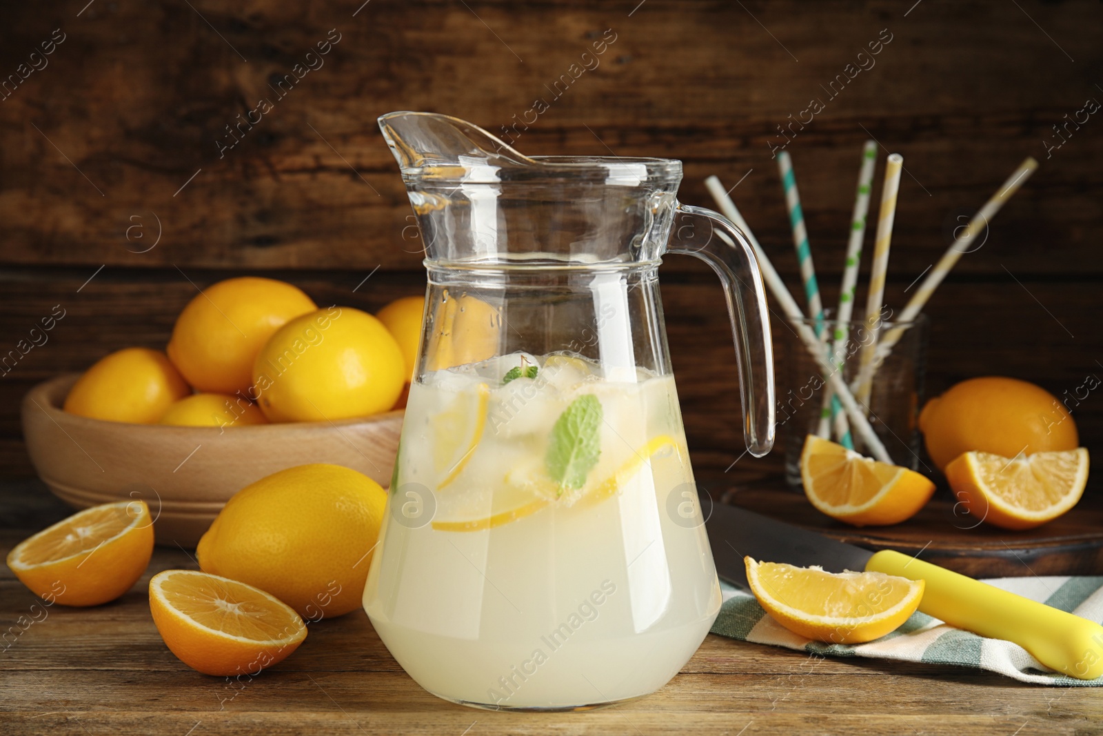 Photo of Cool freshly made lemonade in glass pitcher and fresh fruits on wooden table