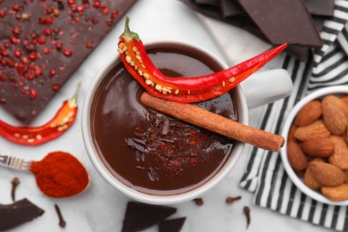 Cup of hot chocolate with chili pepper and cinnamon on white marble table, flat lay