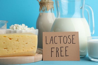 Photo of Dairy products and card with phrase Lactose Free on light blue table, closeup