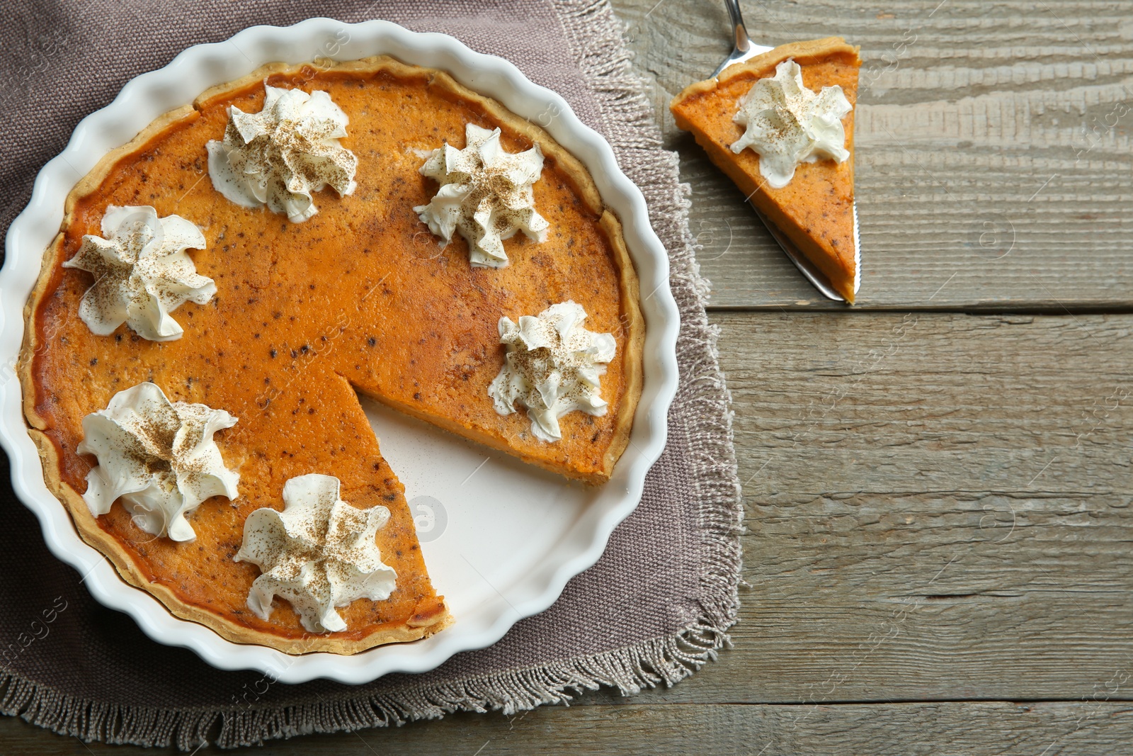 Photo of Delicious pumpkin pie with whipped cream and server on wooden table, flat lay. Space for text