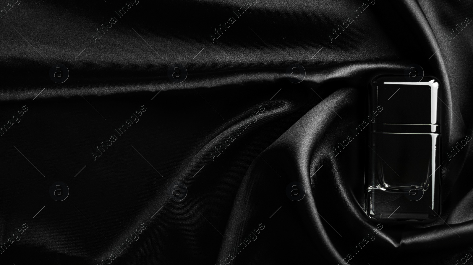 Photo of Luxury bottle of perfume on black silk, top view. Space for text
