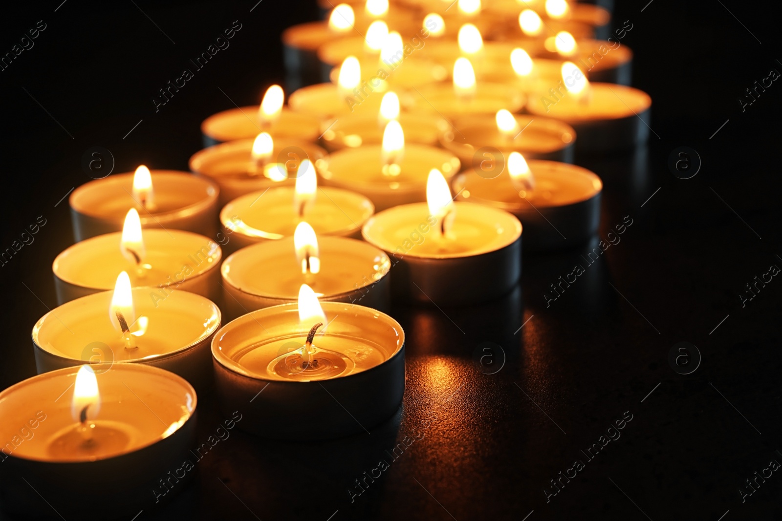 Photo of Wax candles burning on table in darkness, closeup