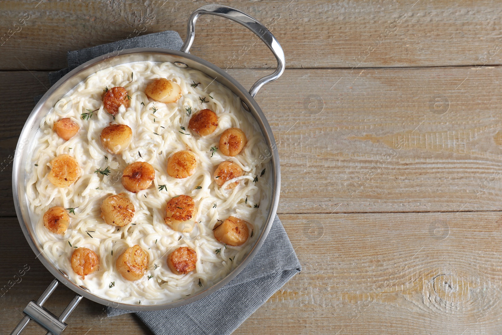 Photo of Delicious scallop pasta in pan on wooden table, top view. Space for text