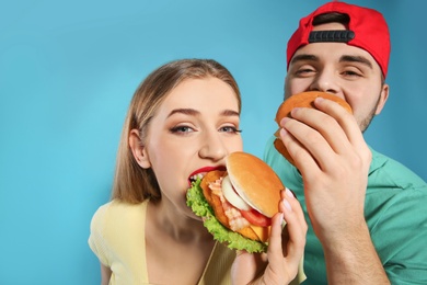 Photo of Happy couple eating burgers on color background