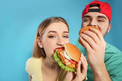 Happy couple eating burgers on color background