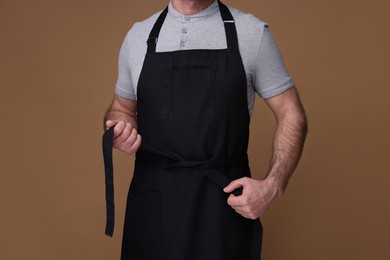 Man wearing kitchen apron on brown background, closeup. Mockup for design