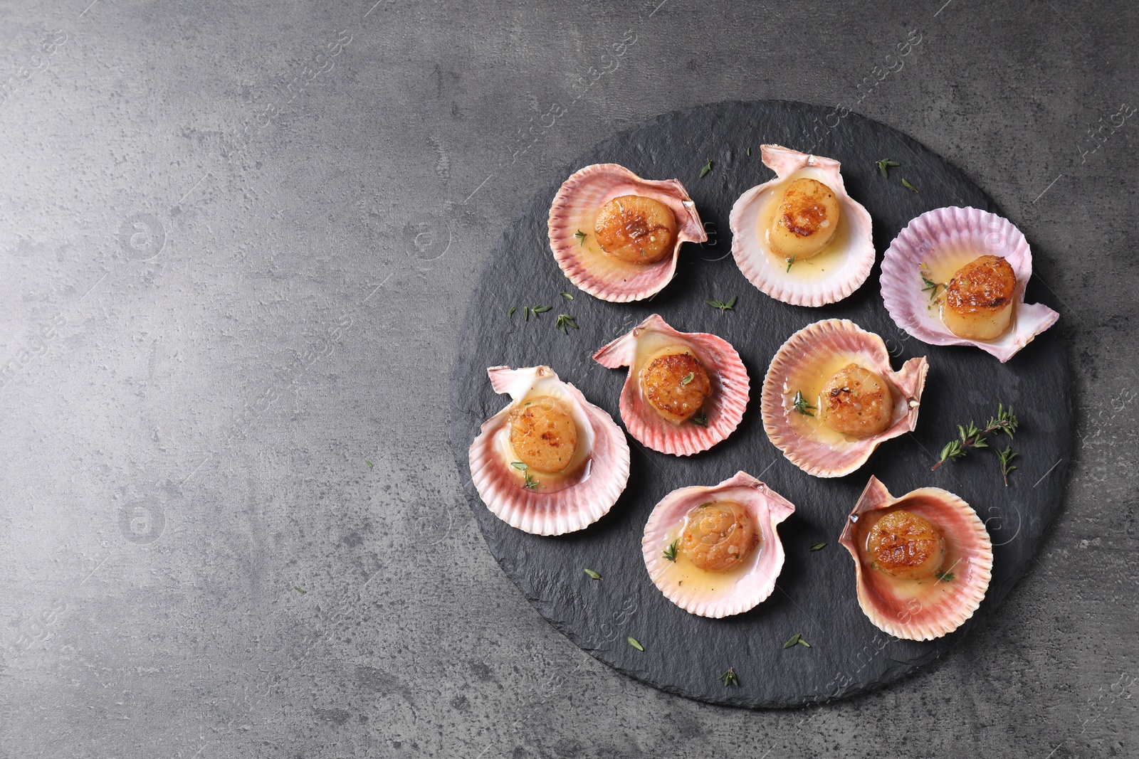 Photo of Delicious fried scallops in shells on grey table, top view. Space for text