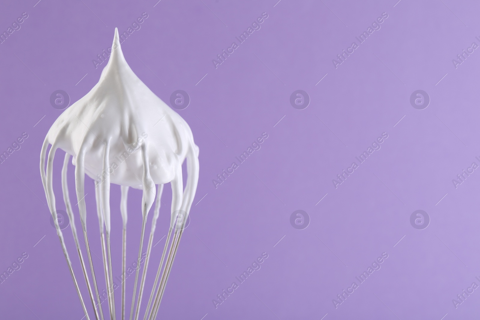 Photo of Whisk with whipped cream on violet background, closeup. Space for text