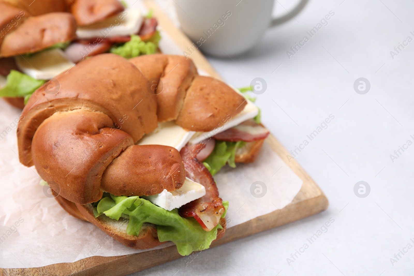 Photo of Tasty crescent roll with brie cheese and bacon on white table, closeup. Space for text