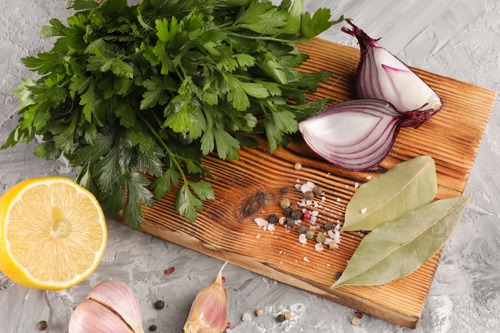 Photo of Bunch of fresh parsley, lemon, onion, garlic and spices on grey textured table, above view